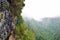 Hikers walking on a narrow path on the edge of the rock during Levada do Caldeirao Verde Trail. Misty green mountains in
