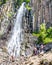 Hikers watching scenic Palisade Falls flowing over steep cliff in a lush Montana forest