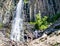 Hikers watching scenic Palisade Falls flowing over steep cliff in a lush Montana forest