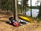 Hiking equipment lies in the sun in the forest by the lake. Kayak, tent, backpack, life jackets, sports mats, barbecue grill.