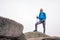 Hiking girl with poles and backpack standing on rocks. Windy autumn day. Travel and healthy lifestyle outdoors in fall season