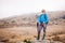 Hiking girl with poles and backpack standing on rocks. Windy autumn day. Travel and healthy lifestyle outdoors in fall season