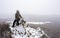 Hiking: a girl sits on a snowy top of a cliff. Overcast and light snow.