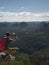 Hiking man with backpack, hat and phone sit on mountain cliff