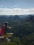 Hiking man with backpack, hat and phone sit on mountain cliff