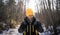 Hiking: A man in a yellow hat goes hiking in a winter forest and carries a large gray backpack. Front view.