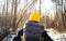 Hiking: A man in a yellow hat goes hiking in a winter forest and carries a large gray backpack. View from the back.