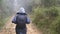 Hiking woman with backpack running in tropical wet forest. Young girl in raincoat jogging on wood trail during travel