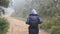 Hiking woman with backpack running in tropical wet forest. Young girl in raincoat jogging on wood trail during travel