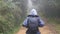 Hiking woman with backpack running in tropical wet forest. Young girl in raincoat jogging on wood trail during travel