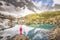 Hiking woman in red clothes stay at beautiful reflection of a lake in mountains.