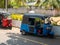 Hikkaduwa, Sri Lanka - March 12, 2022: Blue and red tuk-tuks stand along the road under palm trees
