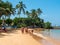 Hikkaduwa, Sri Lanka - March 8, 2022: View of Hikkaduwa beach with green palm trees. Tourists walk along the coast of the Indian