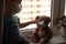 Ð¡hild and his teddy bear both in protective medical masks sits on windowsill