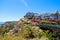 A hillside filled with beachfront homes and a trail along the cliff with large palm trees and lush green trees and plants