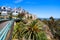 A hillside filled with beachfront homes and a trail along the cliff with large palm trees and lush green trees and plants