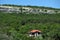 Hillside house among green forest and white layered cliffs blue sky