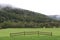 Hillside with low clouds and green meadow with fence section