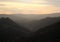 Hillside tree covered valley landscape blurred by fog at sunrise glowing a warm orange color with tops of hills showing in mist