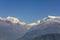 Hillsides with green forests on the background of desert mountains and the snowy ridge of Annapurna under a clear blue sky.