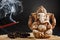 Hindu god Ganesh on a black background. Rudraksha statue and rosary on a wooden table with a red incense stick and incense smoke