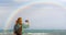 A hippie blogger girl takes pictures of a rainbow on a mobile phone. Beauty over the sea. The concept of travel