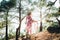 A hippie girl in a beautiful flying dress, hat and round glasses in a pine forest among the mountains.