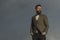 Hipster with beard and mustache on unshaven face. Bearded man on cloudy sky. Fashion businessman wear classic coat with