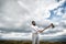 Hipster with beard on strict face holds axe, cloudy sky background. Man with beard holds axe while stand on top of