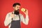 Hipster bearded baker hold glazed donut on red background. Cafe and bakery concept. Sweet donut from baker. Man bearded