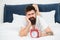 Hipster bearded man lay in bed with alarm clock. Time to wake up. Why you should wake up early every morning. Health