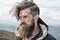 Hipster, bearded man on mountain top on natural cloudy sky