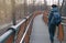 Hipster bearded millennial man in classic blue jacket with backpack walking on modern wooden path in the winter or autumn park.