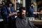 Hipster client getting haircut. Barber with clipper trimming hair on nape of client. Barber with hair clipper works on