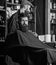 Hipster client getting haircut. Haircut process concept. Man with beard covered with black cape waiting while barber