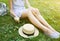 Hipster girl is holding melting ice-cream in hands. Woman sitting on green grass with straw hat. Cold summer desserts. Hot weather