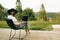 Hipster girl with laptop sitting on wooden porch with beautiful view on woods and mountains. Stylish Young woman in hat using