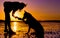 Hipster girl playing with dog at a beach during sunset, silhouettes