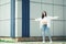 Hipster girl wearing blank white t-shirt, jeans and sunglasses posing against rough street wall, minimalist urban clothing style.