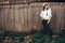 Hipster girl in white casual outfit posing on background of old wooden cabin in mountains. Stylish woman in hat standing near old