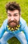 Hipster on happy face sits on grass, defocused. Man with beard enjoys spring, green meadow background. Guy with lesser