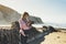 Hipster hiker tourist with backpack taking photo of amazing seascape sunset on camera on background mountains, photographer enjoy