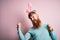 Hipster Irish man with beard wearing easter rabbit ears over isolated pink background very happy and excited doing winner gesture