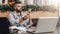 Hipster man sits in cafe, uses smartphone, works on two laptops. Businessman reads an information message in phone.