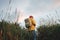 Hipster man traveler wearing backpack and yellow raincoat hiking among high grass