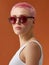 Hipster pinkhead girl in red sunglasses on brown background
