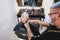 Hipster senior man getting hair cut with a razor and clipper in vintage barbershop - Barber wearing protective mask for