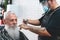Hipster senior man getting hair cut at vintage barber shop - They both wear face protective masks for coronavirus prevention -