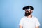 Hipster on smiling face enjoy virtual reality with gadget. Man with beard in VR glasses, light blue background. Guy with