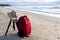 Hipster tourist red backpack with hat and tripod camera on beach